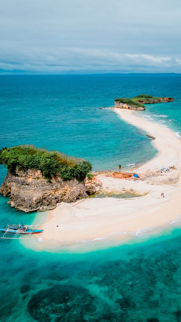 Explore a breathtaking aerial view of a pristine beach in the Philippines, showcasing vibrant blue waters and lush greenery.