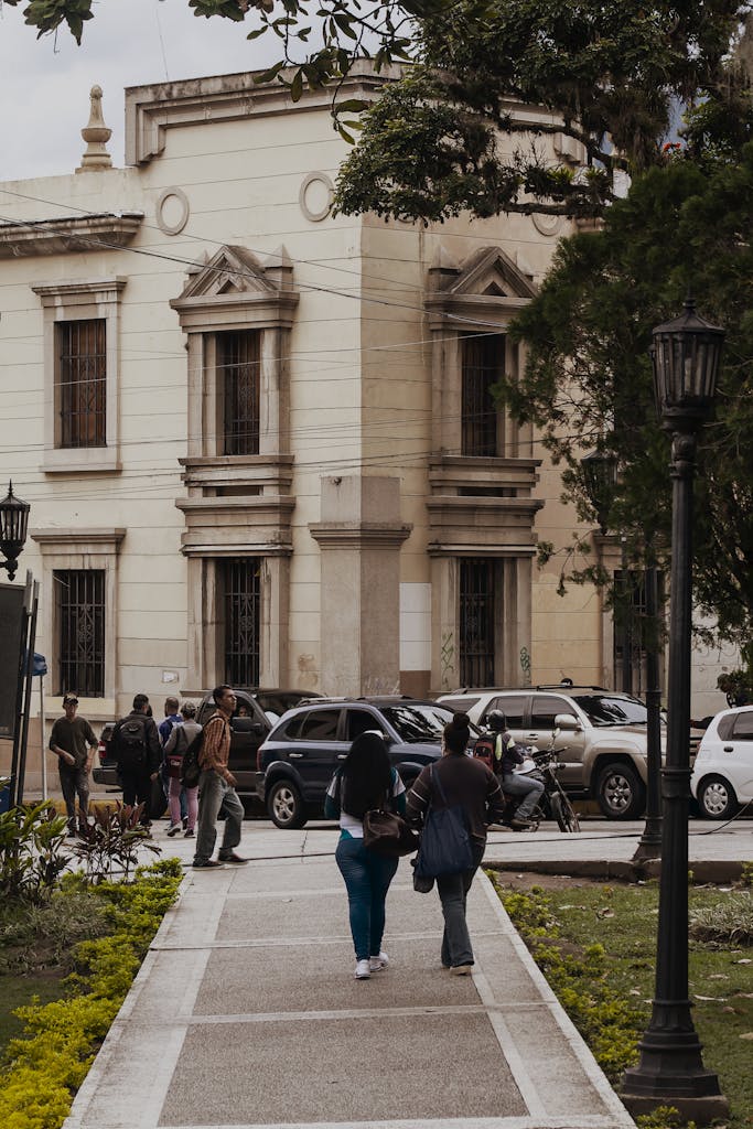 People walking on a street in Mérida, Venezuela, featuring historic architecture and parked cars.